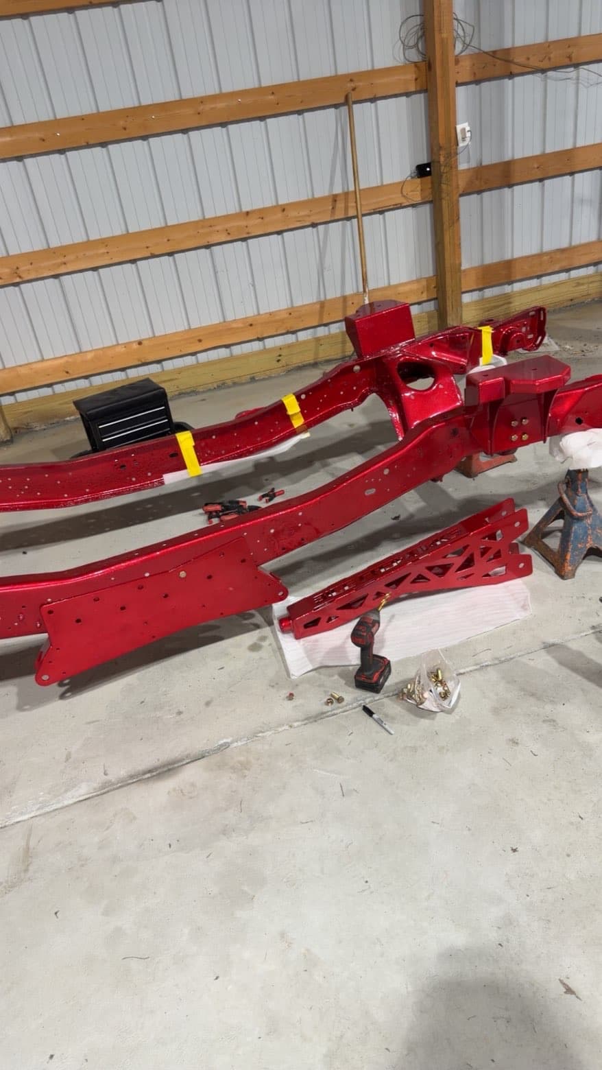 Red powder coated frame rails and suspension components laid out in shop — TP Customs LLC
